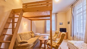 Une pièce chaleureuse avec un lit en mezzanine en bois, un canapé, un fauteuil et une petite table.