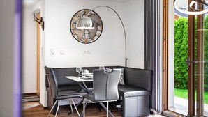 A modern dining area with a round wall clock, a table with chairs, and a view through a glass door.