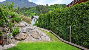 A stone wall, a wooden fence, and a house with a mountain in the background.