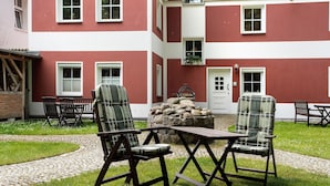 Un patio con mesas al aire libre, un muro de piedra y un edificio con paredes exteriores rojas y blancas.