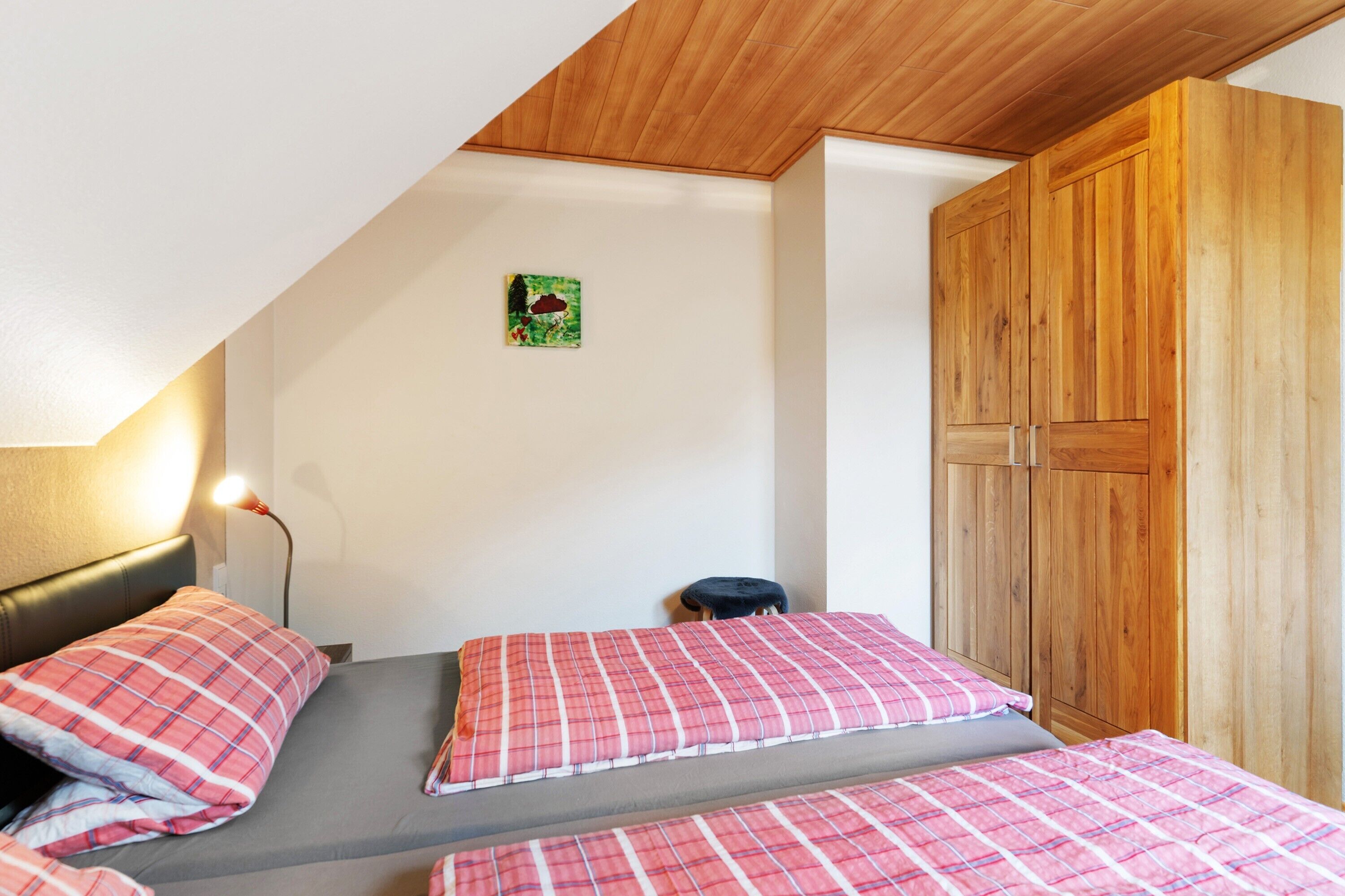 A bedroom with two beds, a wooden wardrobe, a wall-mounted artwork, and a bedside lamp.