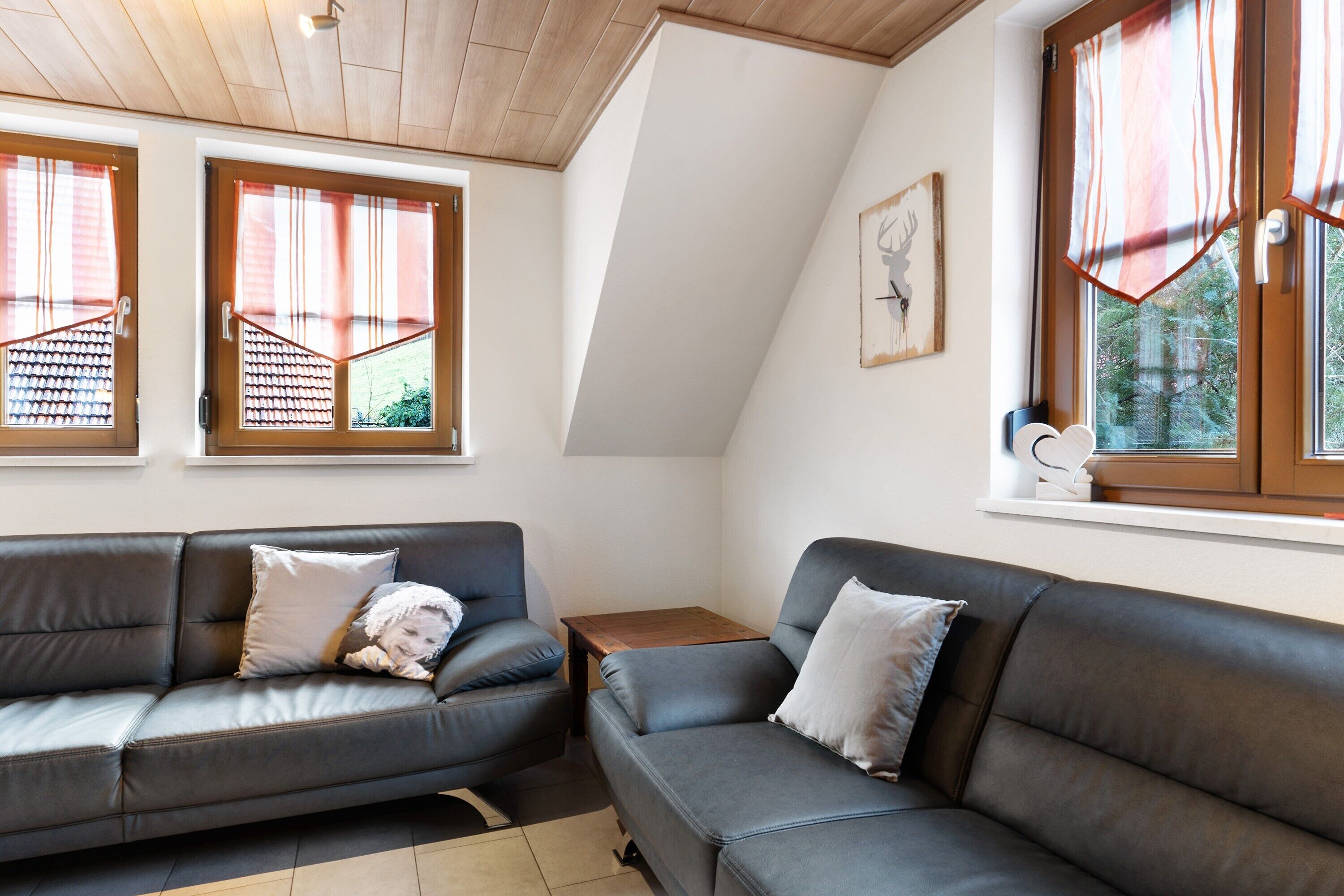 Un salon moderne avec deux canapés gris, une table en bois et de grandes fenêtres avec des rideaux.