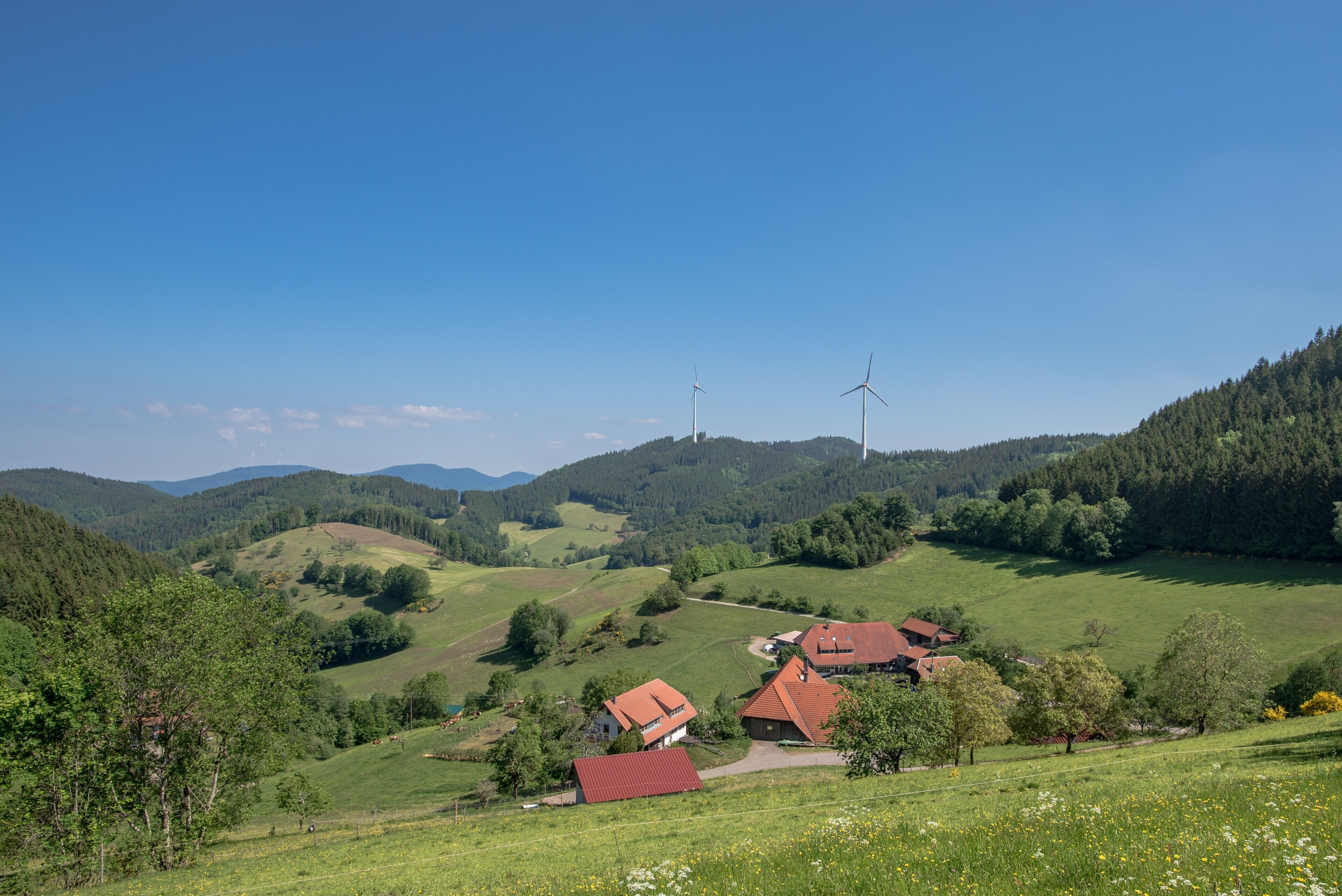 Ett lantligt landskap med böljande kullar, en liten by och vindkraftverk i fjärran.