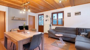 Un intérieur moderne avec un plafond en bois, un coin repas comprenant une table et des chaises, un canapé gris et une petite table ronde.