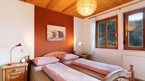 Une chambre avec deux lits, des têtes de lit en bois, une table de chevet avec une lampe, un tableau au mur et une fenêtre donnant sur des arbres.