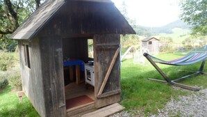 Une structure rustique en bois, dotée d’un toit en pente, d’un petit porche et d’un hamac à l’arrière-plan.