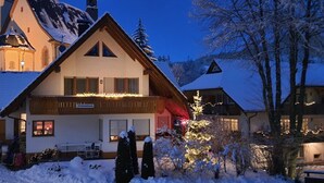 A two-story chalet with a balcony, snow-covered surroundings, and a mountain backdrop.