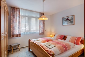 Un dormitorio con cama, mesita de noche, lámpara, ventana con cortinas y un cuadro en la pared.