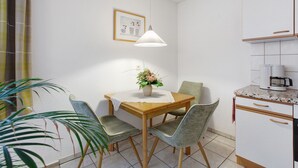 A dining area with a wooden table, four chairs, a potted plant, a hanging light fixture, and a kitchen area with cabinets and a countertop.
