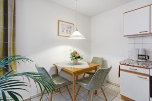 A dining area with a wooden table, four chairs, a potted plant, a hanging light fixture, and a kitchen area with cabinets and a countertop. - Apartment 'Ferienwohnung Matt' with Private Terrace and Wi-Fi (Todtmoos)