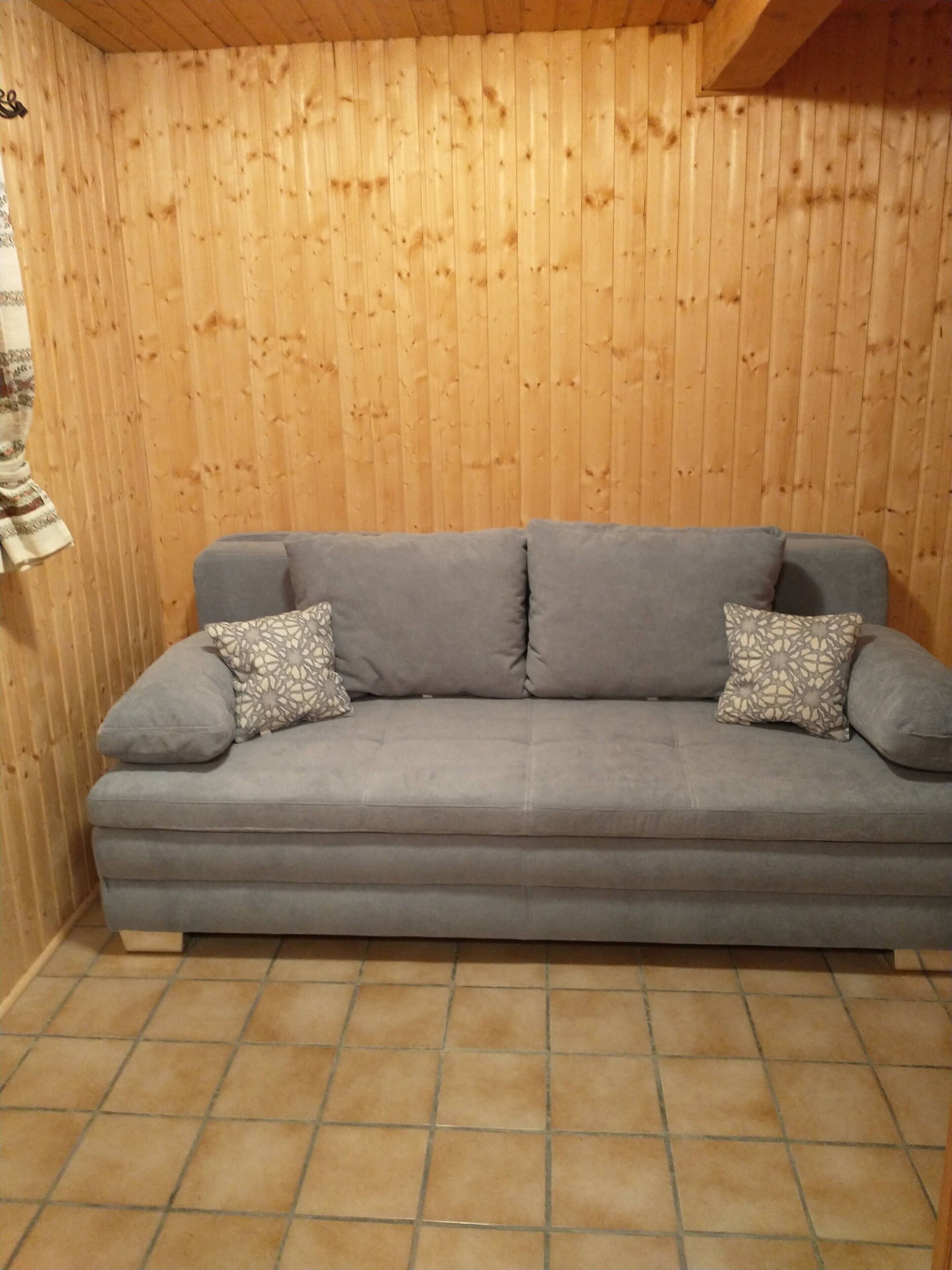 A grey sofa with patterned cushions against a wooden wall with vertical planks.