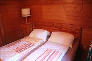 Ein Zimmer einer Holzhütte mit zwei Betten, einem Nachttisch mit Lampe und einer Holzwand.