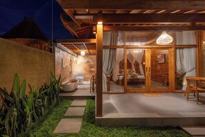 A well-lit outdoor area with a wooden pergola, a stone pathway, and a seating area with a table and chairs. - The Patra Villa (Sebatu)