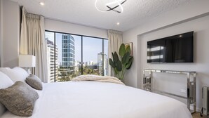 A modern hotel room with a large bed, a flat-screen TV, a large window with a city view, and a plant. - Seaview balcony King Pacific Ocean Larcomar (Miraflores)