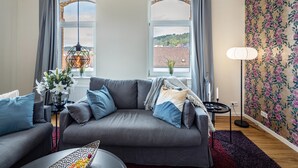 A modern living room with a grey sofa, a small side table, a floor lamp, and a view through large windows. - Apartment 'Residenz Unter Der Birke - Esche' with Mountain View, Shared Terrace and Wi-Fi (Eisenach)