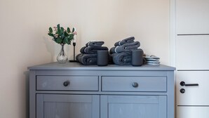 A grey cabinet with two drawers, a vase with green leaves, and a stack of folded towels and a black mug. - Apartment 'Residenz Unter Der Birke - Esche' with Mountain View, Shared Terrace and Wi-Fi (Eisenach)