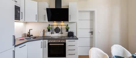 A modern kitchen with white cabinetry, a black oven, a built-in microwave, and a flat-screen TV above the stove.