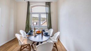 A dining area with a round table, white chairs, a window with curtains, and a view of a building. - Apartment 'Residenz Unter Der Birke - Esche' with Mountain View, Shared Terrace and Wi-Fi (Eisenach)