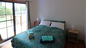 Ein Schlafzimmer mit Bett, Nachttisch, Pendelleuchte und Blick durch ein großes Fenster.