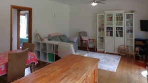 Ein Wohnzimmer mit Holztisch, Stühlen, einer Couch, einem Bücherregal und einem Deckenventilator.