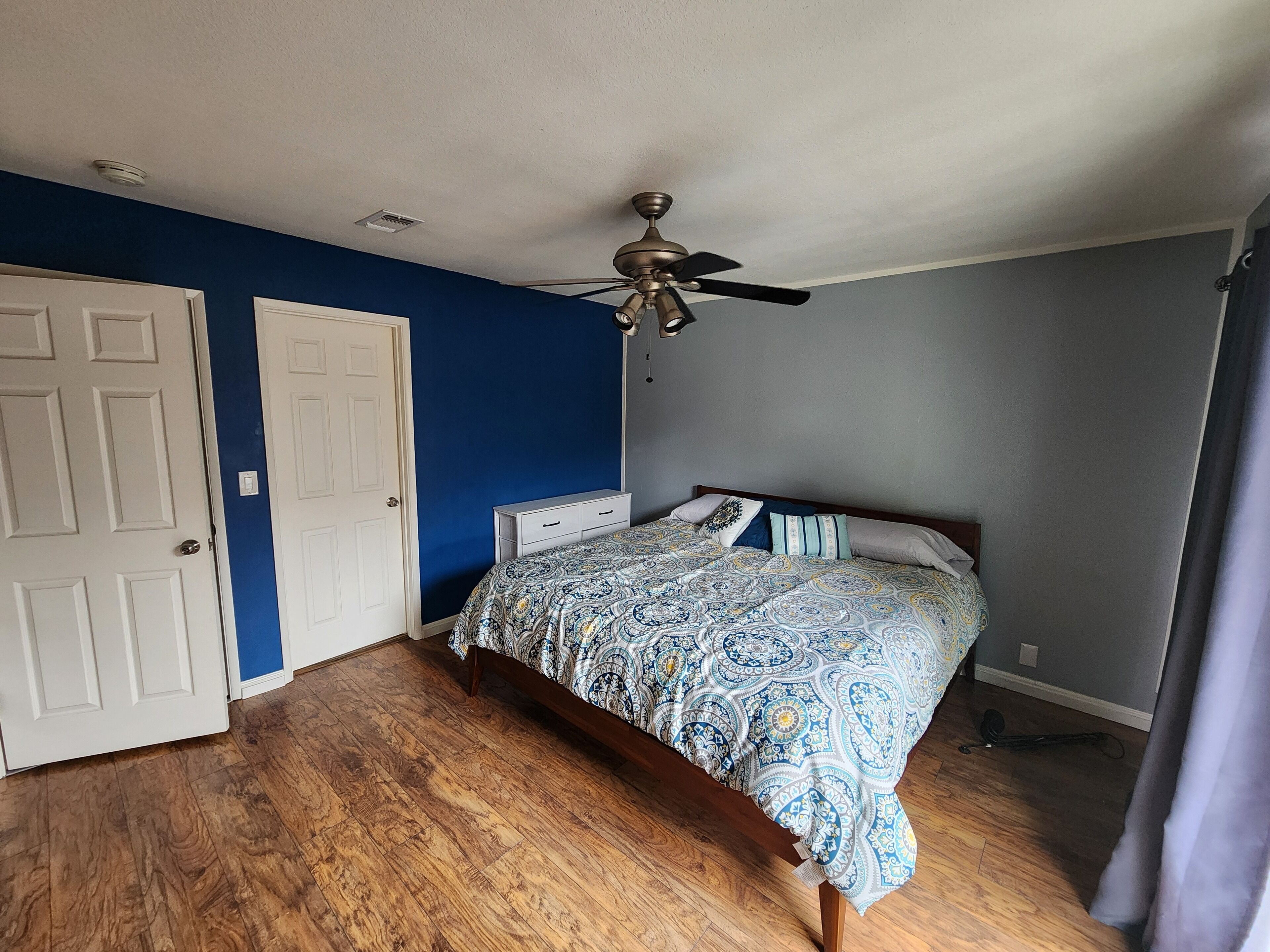A bedroom with a bed, a ceiling fan, and wooden flooring.