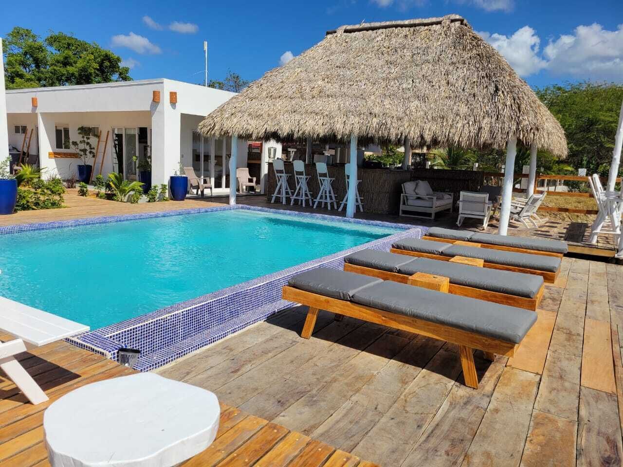 A pool area with lounge chairs, a thatched-roof structure, and a wooden deck.