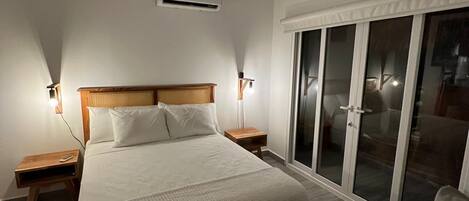 A bedroom with a large bed, two bedside tables, a nightstand, a ceiling fan, and a sliding glass door leading to a balcony.