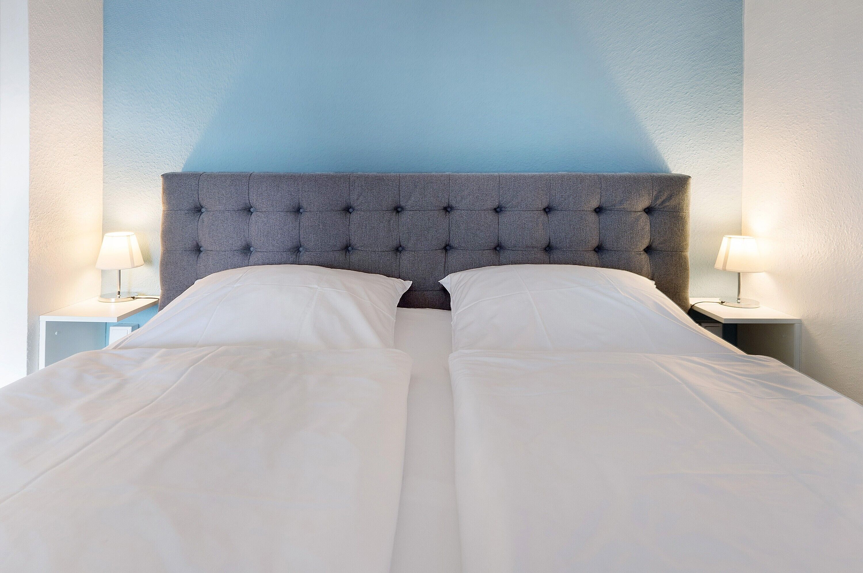 A bed with a tufted headboard, white bedding, and two bedside lamps on nightstands.