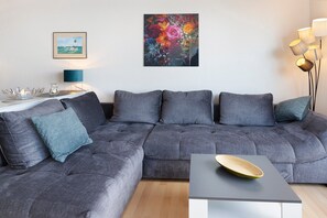Ein graues Ecksofa mit Kissen, ein kleiner Tisch mit einer Schüssel, ein gerahmtes Bild und eine Stehlampe.