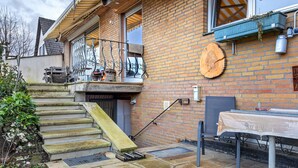 A brick house with a wooden staircase, a table with a tablecloth, and a metal chair.