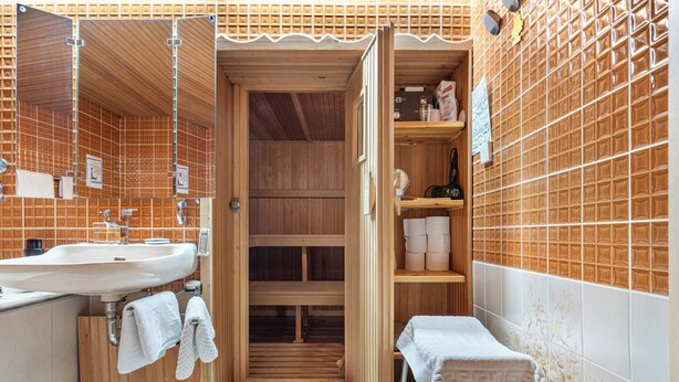 A bathroom with a wooden vanity, a sink, and a mirror. There is a towel rack and a shelf with toiletries.