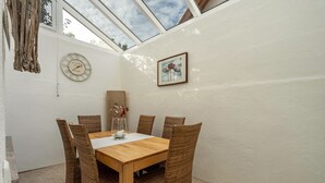 Ein Essbereich mit einem Holztisch und Korbstühlen, einer Uhr an der Wand und einem gerahmten Bild.