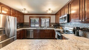 A modern kitchen with wooden cabinets, stainless steel appliances, and a marble countertop. - Central Tahoe Retreat | Lake Views + Walk to Shore (Tahoe City)
