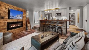 Una sala de estar moderna con chimenea, televisor y una zona de bar con taburetes.