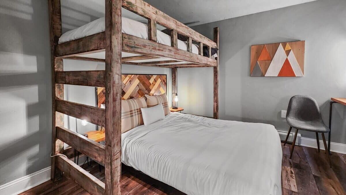A bunk bed with a wooden headboard, a bedside table with a lamp, and a chair.