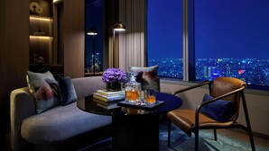 Una sala de estar moderna con sofá, mesa de centro, una silla y vistas a un paisaje urbano nocturno.