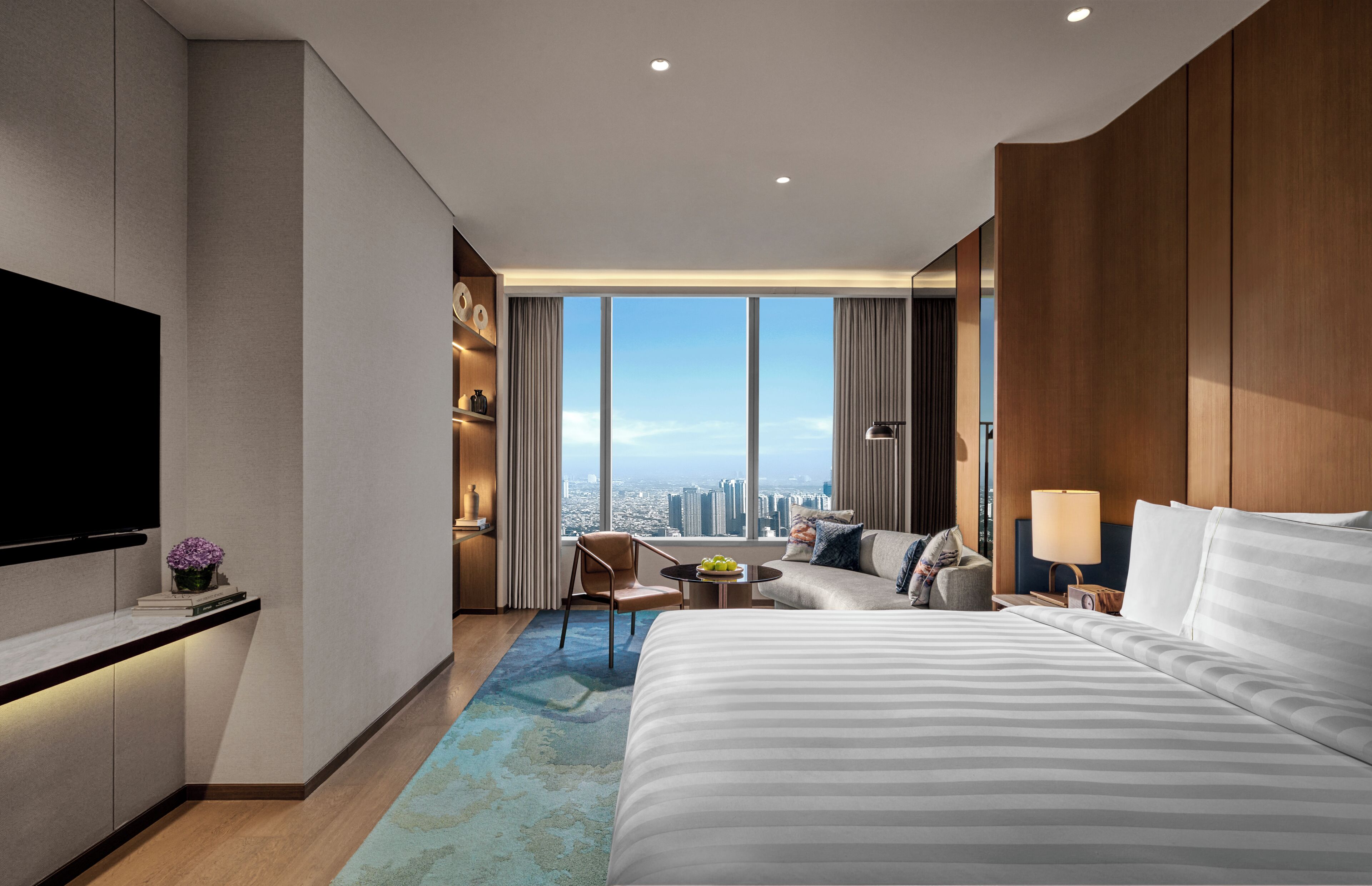Une chambre d’hôtel moderne dotée d’un grand lit, d’une télévision, d’un canapé, d’un fauteuil, d’une petite table et offrant une vue sur la ville.