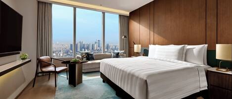 A modern hotel room with a large bed, a seating area, a TV, and a city view.