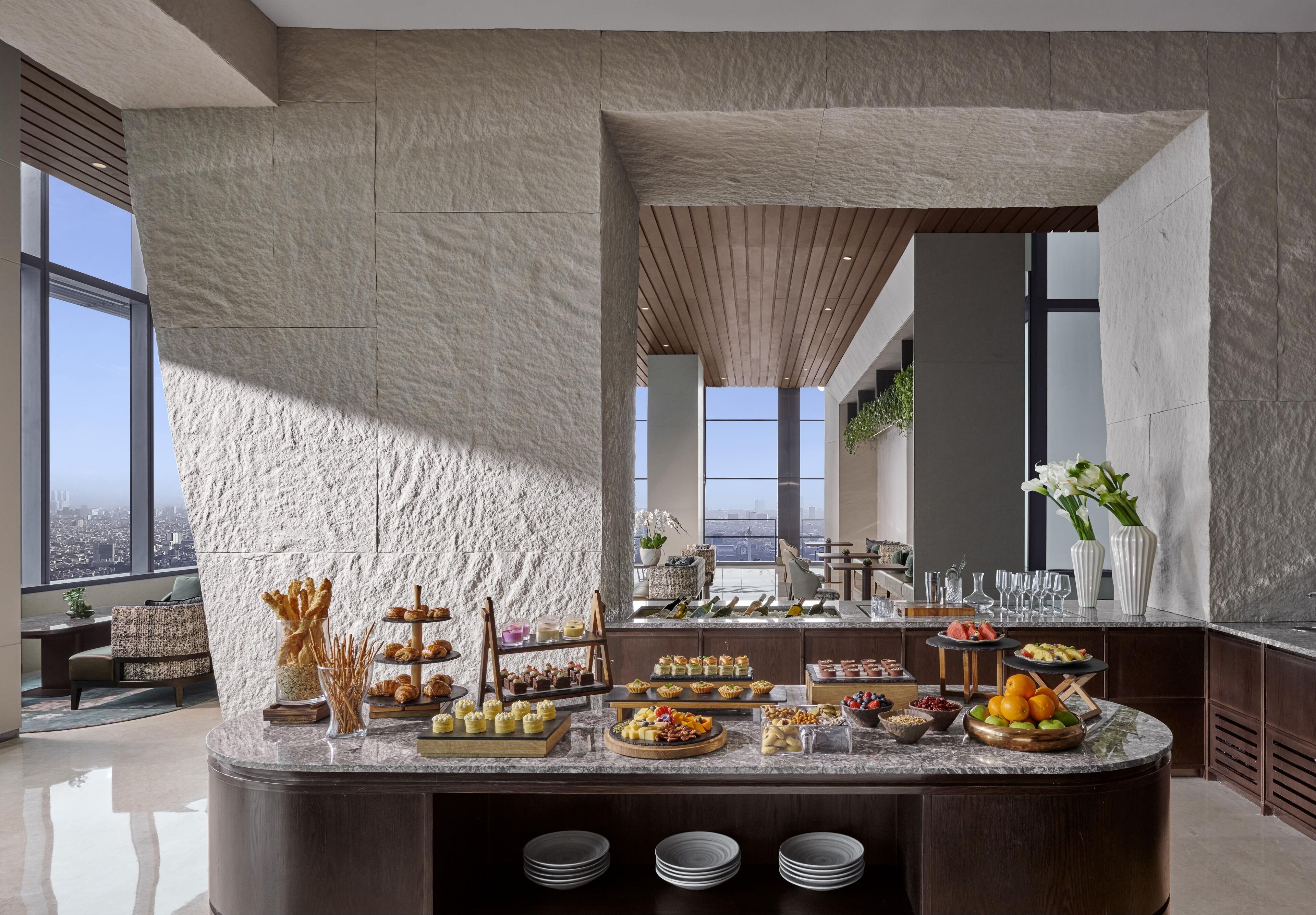 Un somptueux buffet de petit-déjeuner proposant une grande variété de viennoiseries, de fruits et de boissons, le tout dans un cadre moderne agrémenté de grandes fenêtres et offrant une vue sur la ville.