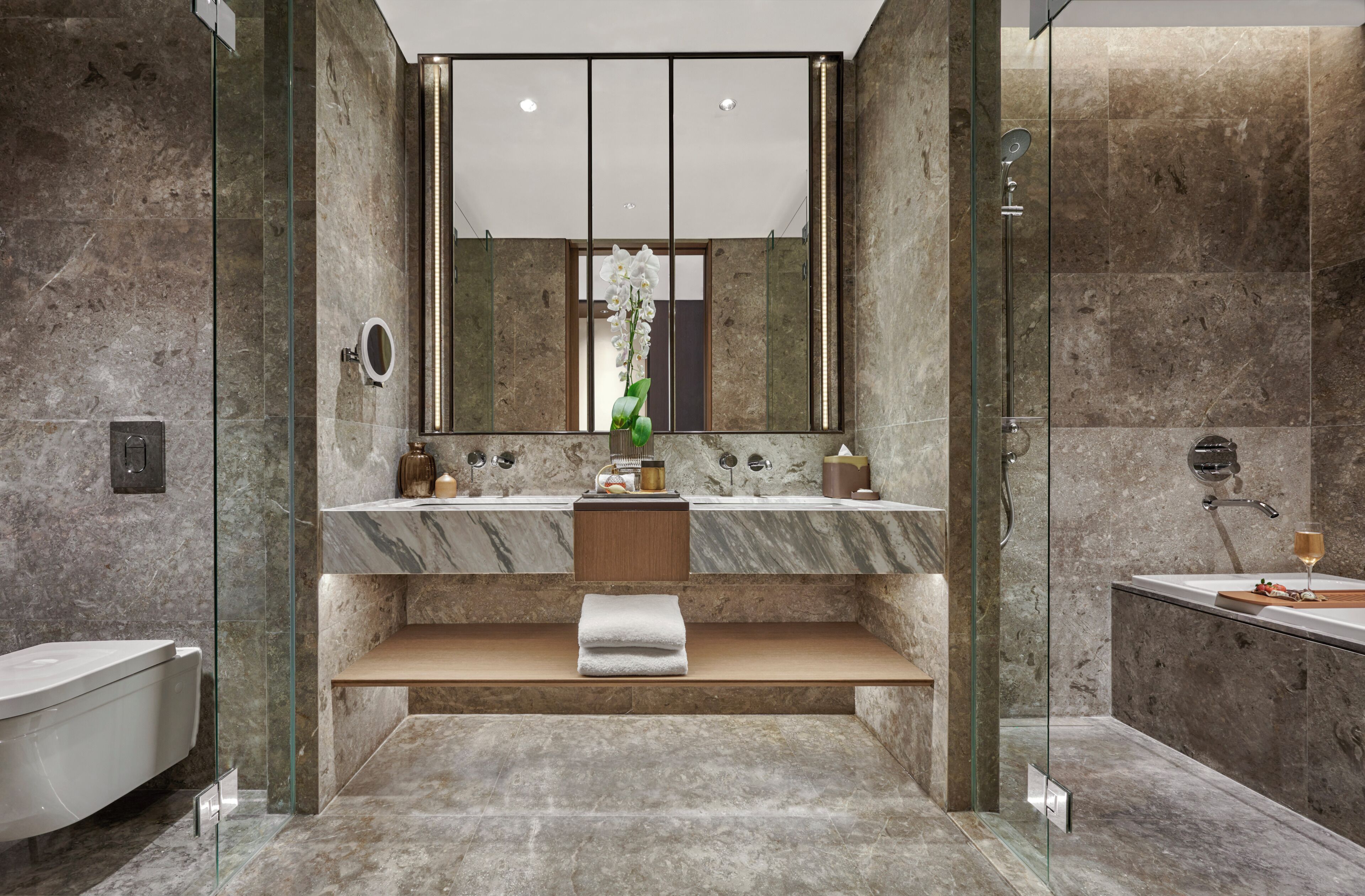 Un baño moderno con ducha de vidrio, tocador de mármol y un espejo grande.