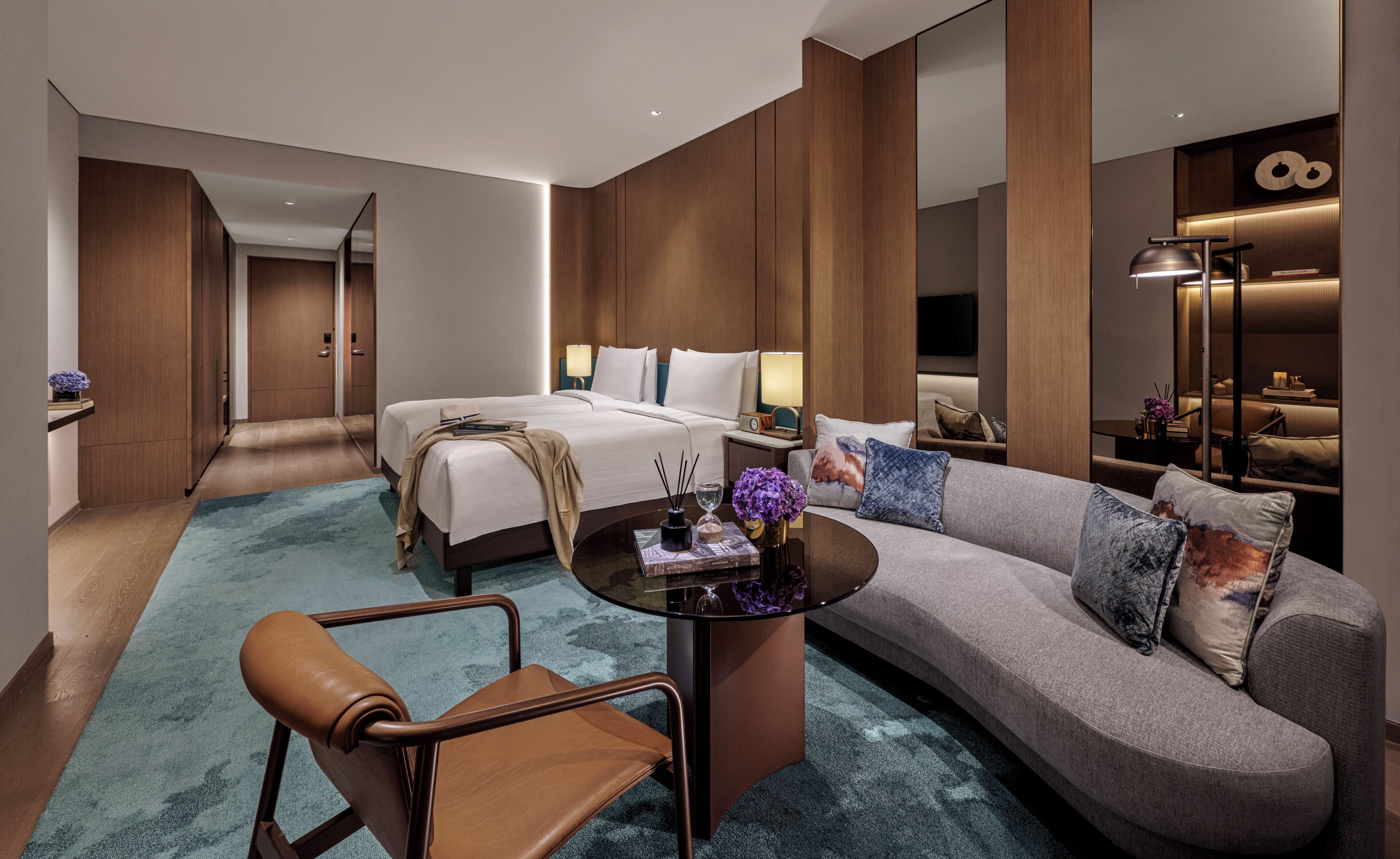 A modern hotel room with a bed, sofa, coffee table, and a chair.