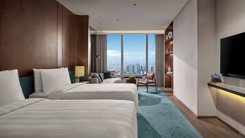 Habitación de hotel con dos camas, un escritorio, una silla, un televisor y vistas a la ciudad.