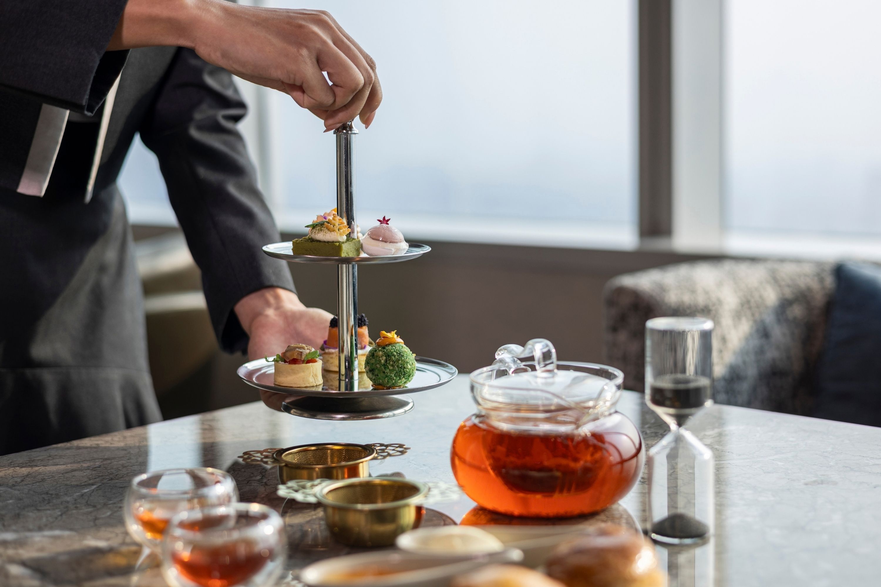 Une personne présente un dessert à étages sur une table, avec une théière et des verres.