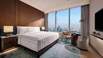 A hotel room with a large bed, a desk, a chair, a TV, and a view of the city skyline.