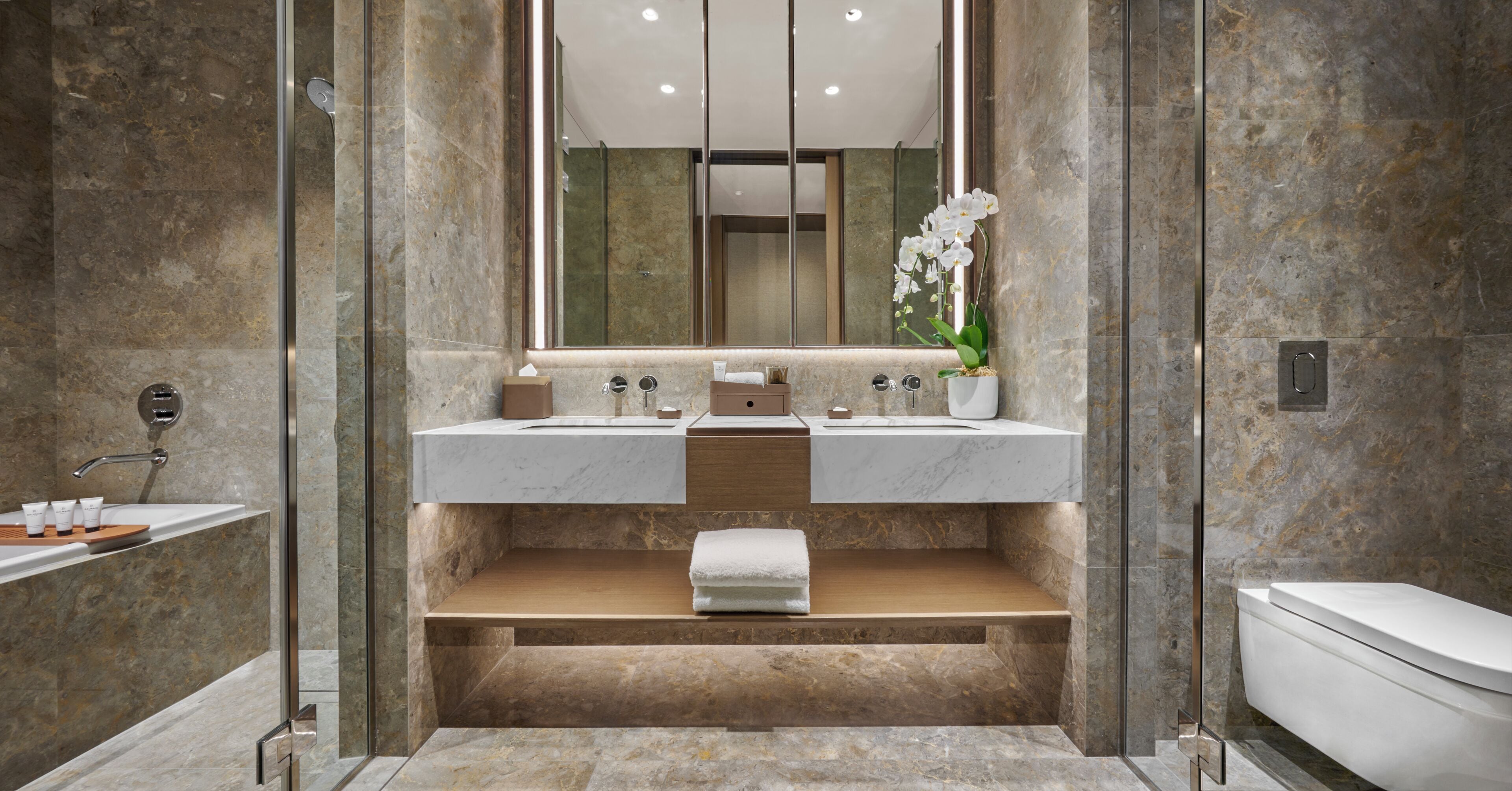 Un baño moderno con un espejo grande, dos lavabos, ducha e inodoro.