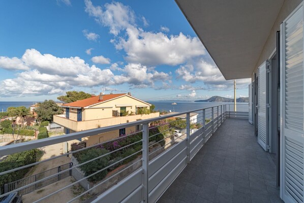 A balcony with a view of a coastal area, including a building with a red roof and a body of water in the distance.