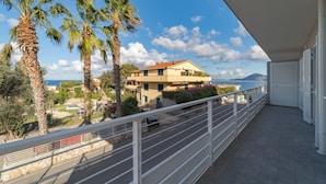 Un balcon offrant une vue sur un bâtiment situé sur la côte, des palmiers et un ciel dégagé.