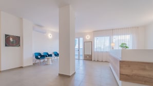 Un amplio y moderno vestíbulo de hotel con una recepción, sillas azules y un gran ventanal con cortinas.