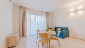 Una sala de estar moderna con una mesa de comedor, sillas, un sofá azul y un pequeño armario de madera.