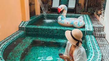 A person sitting by a small pool with a flamingo float, surrounded by a tiled patio with a tray of food and drinks.